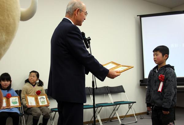 市長がマイクの前で上川 敦也（かみかわ あつや）さんを表彰している写真