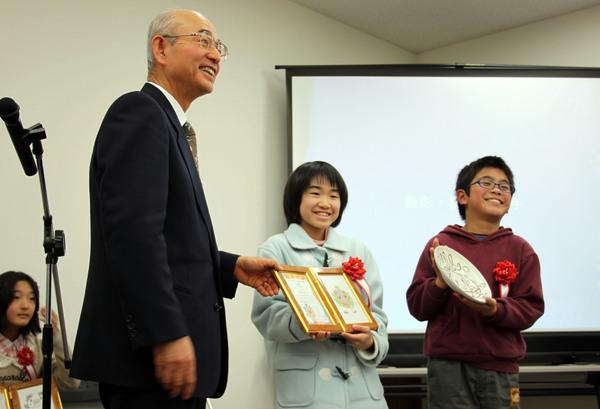 くりんが描かれたお皿を持っている男の子と額に入った賞状を持っている女の子が市長とならんで写した写真