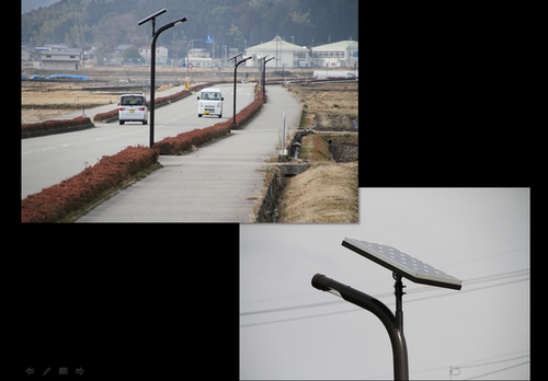 道路を車が2台走っていて、歩道にソーラーパネル付きの外灯が設置されている写真