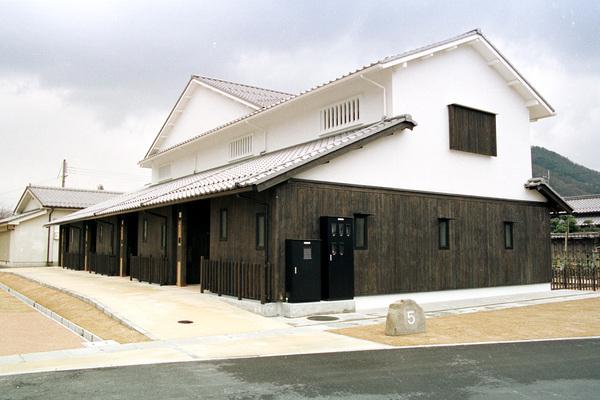 一階の壁が茶色で、二階の壁が白色に塗装された、横長い2階建ての家屋が立っている写真