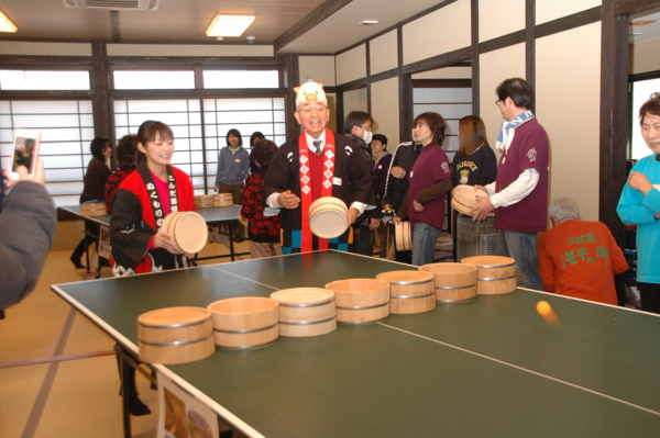 法被を着たふるさと大使の熊谷 奈美さんと法被とまるいのの紙のお面をつけた市長が相手の陣地に玉が入って喜んでいる写真
