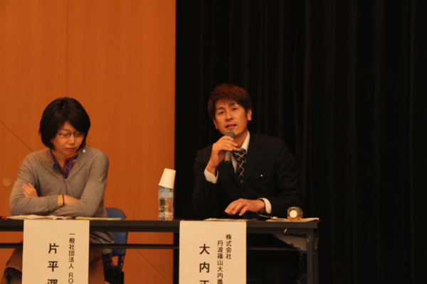 マイクを持った大内 正博さんが椅子に座りながら発表し、その横で片平 深雪さんが腕を組み、資料に目を通している写真