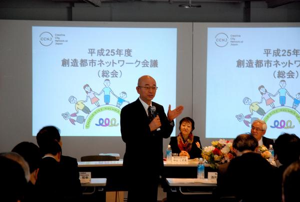 会議参加者が着席している席の間で、市長がマイクを持って話をしている様子の写真