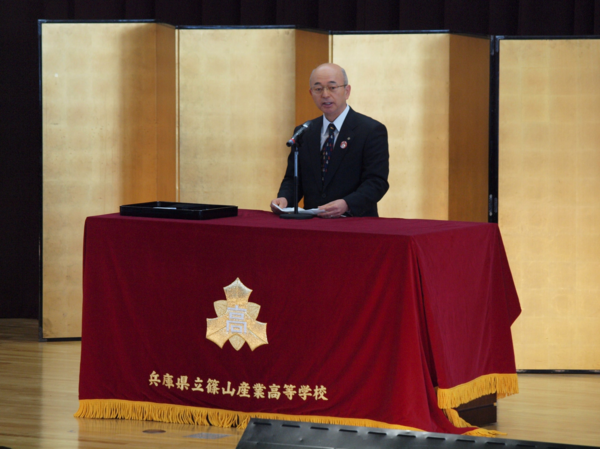 ステージ上の壇上で市長が卒業生に向けて祝辞を述べている写真