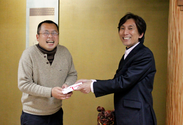 笑顔の神戸新聞社の井原 尚基記者とスーツを着た男性が一緒に封筒を持っている写真