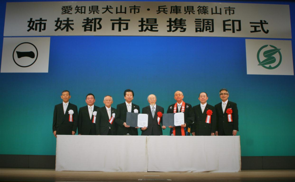 「姉妹都市提携調印式」の横断幕の下で8名の関係者が並んでの記念撮影の写真