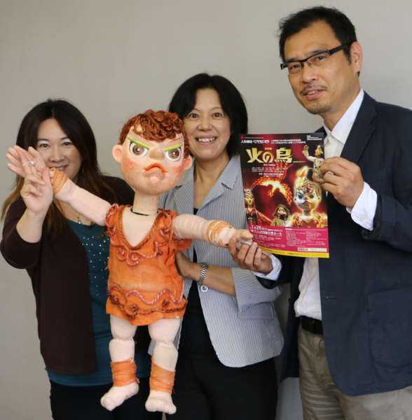 火の鳥のチラシと人形を持った男女3名が記念撮影している写真