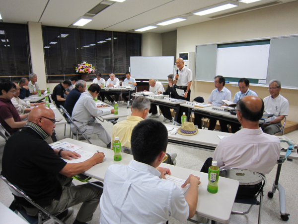 城北会場で参加者は椅子に座り、テーブルには資料とお茶が置かれていて、前で市長が立って話をしている写真