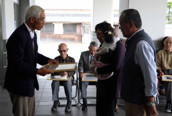 飼い主の男性と犬を抱いている女性が獣医師会長より表彰していただいている写真