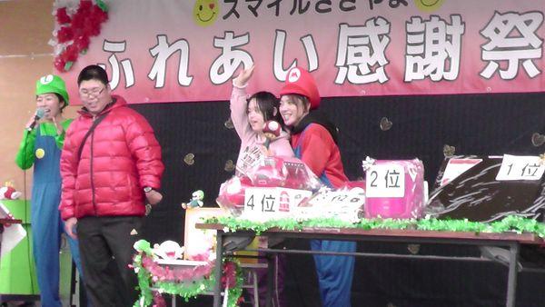 舞台の上でルイジーがの格好をした女性司会者が話をして、マリオの格好をした女性は女の子とふれあっている写真