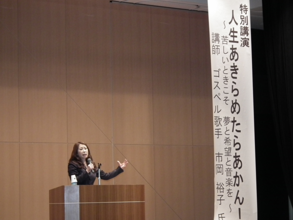 特別講演「人生あきらめたらあかん！」でマイクを手に持ち一生懸命話している市岡裕子氏の写真