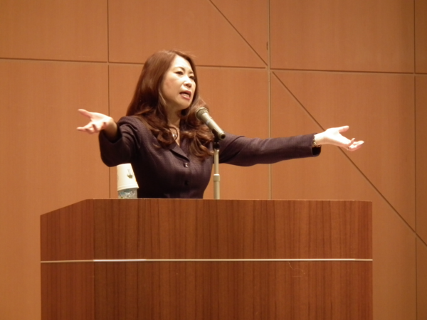 特別講演でマイクを立てて両手を広げて一生懸命話している市岡裕子氏の写真