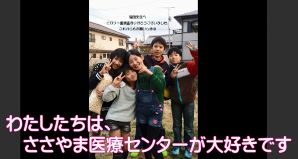 女の子3人が顔をくっつけて笑顔でピースしている後ろで男の子がピースして写っている写真