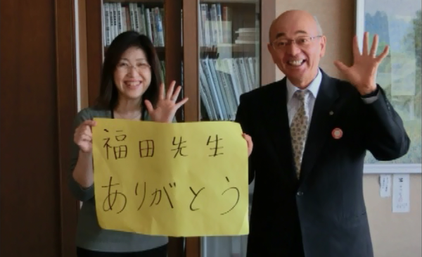 市長と眼鏡をかけた女性がメッセージカードを持って笑顔で片手を上げて写っている写真