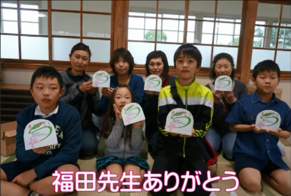 1列名に子供達、2列目に保護者が座ってお互いメッセージカードを持って写っている写真