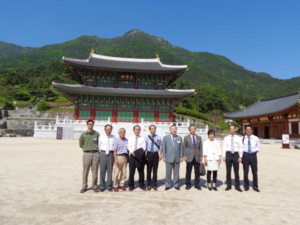 青空の下、山と韓方体験場をバックに篠山市訪問団10名が記念撮影している写真