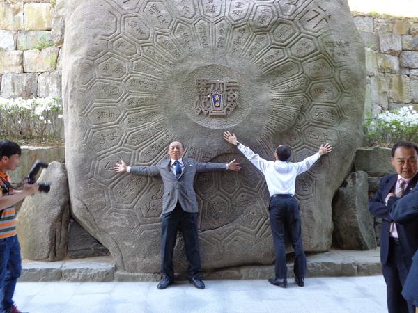 亀の甲羅のような巨石に両手を広げて体をくっつけて写っている男性2名の写真