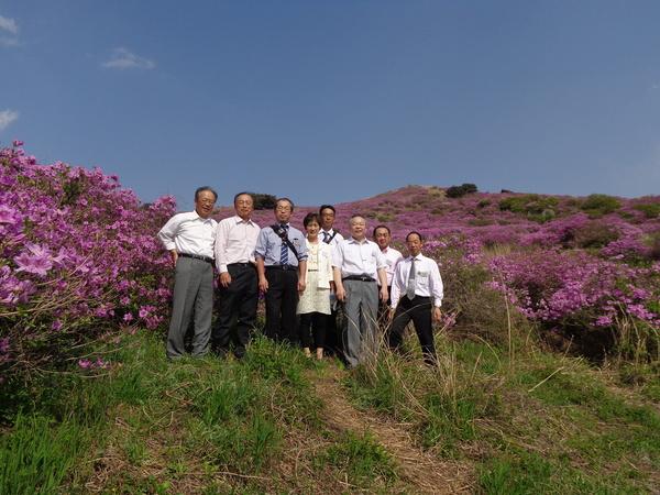 高原一面に咲き誇るツツジの花をバックに記念撮影している写真