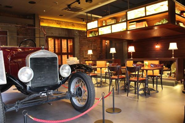 テーブルや椅子の前に赤いクラシックカーが展示されている写真