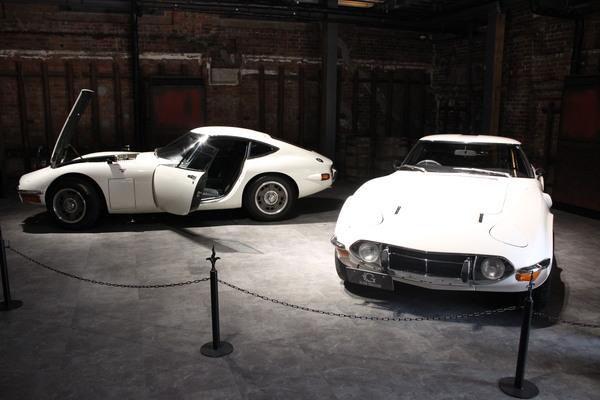 建物の中に白のクラシックカーが二台、展示されていて、一台はドアとボンネットが開いている写真