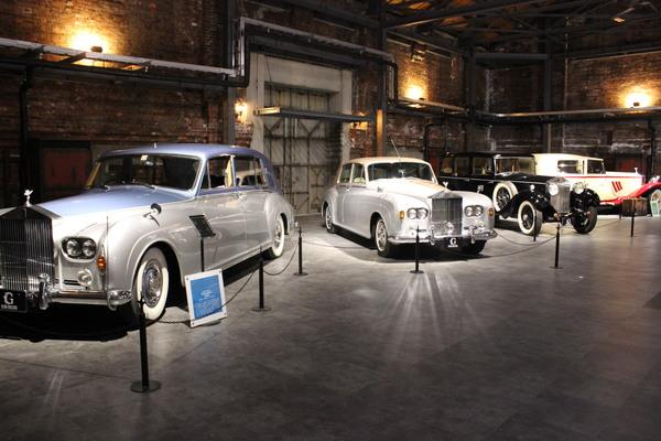 灰色の床の建物の中でシルバーや黒の4台のクラシックカーが展示されている写真