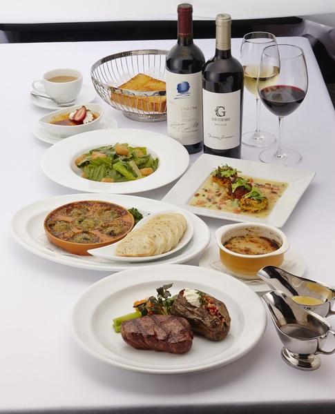白いテーブルの上にステーキなどの料理やワインが並べてある写真