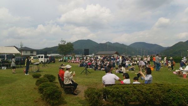 司会者の方が、広場の芝生に座っているお客さんにお話ししている写真