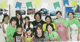 教育フェスティバルに参加した外国の親子と後方にエプロンと三角巾をした女性3名の集合写真