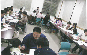 長机に2名の外国人に対し1名の指導者が対面式で座り教えている日本語教室会場の写真