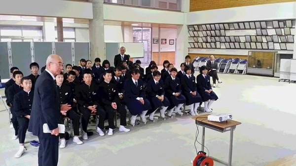 武道場に並んだ椅子に生徒達が座ってプロジェクターで映し出された映像を見ながら市長の話しを聞いている写真