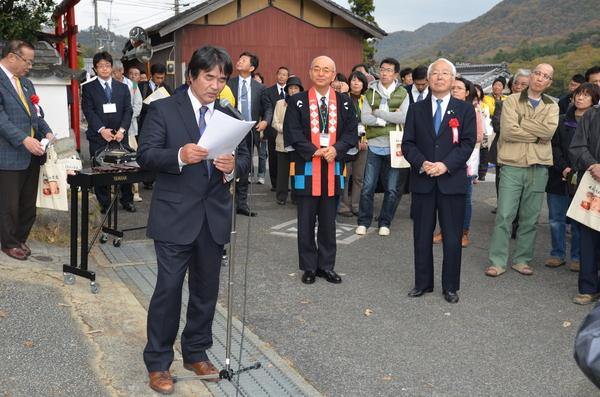 市野組合長がスタンドマイクを使い、みんなの前でお話しして様子を周りで市長や住民の方が聞いている写真