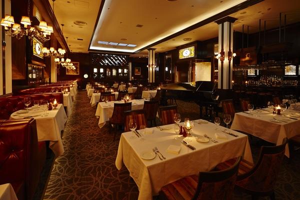 照明の落ちたレストランの中でたくさんのテーブルの上に蝋燭やお皿、フォーク、グラスなどがセッティングされている写真