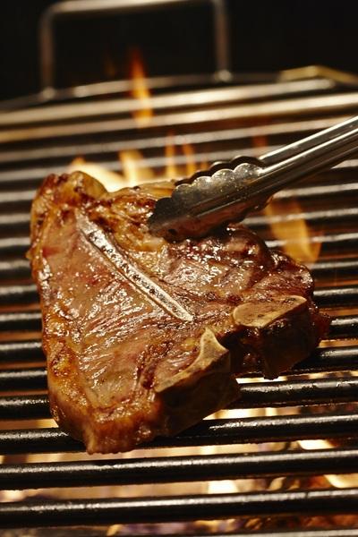 網の上でステーキが焼かれていてトングで裏返そうとしている写真