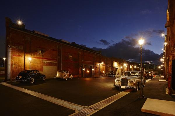 街灯が光る夜に茶色い建物の前に5台のクラシックカーが展示されている写真