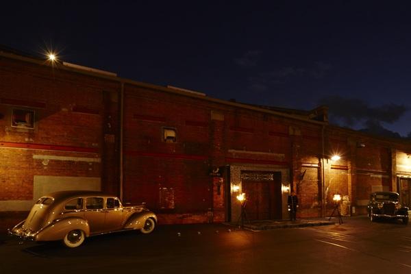 茶色い建物の手前にシルバーのクラシックカーと奥に緑のクラシックカーが停まっている写真