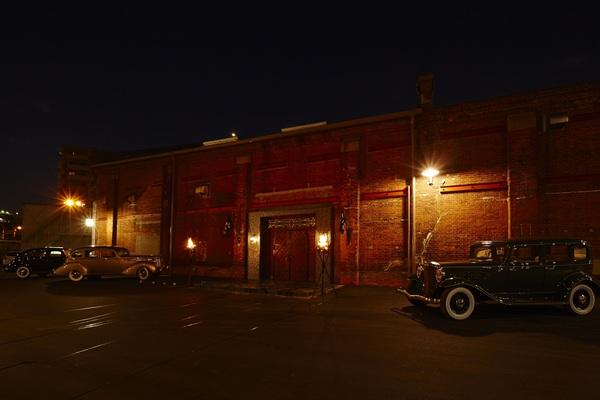 建物の右手に緑のクラシックカーと左の奥に茶色と黒のクラシックカーが展示されている写真