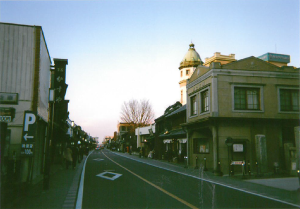 薄暗い中、建物が建ち並んで歩道には人が歩いている写真