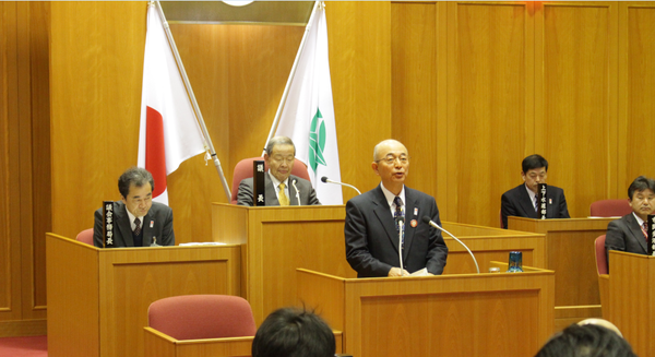 市長が議会で答弁し、周りの議員が聞き入っている様子の写真