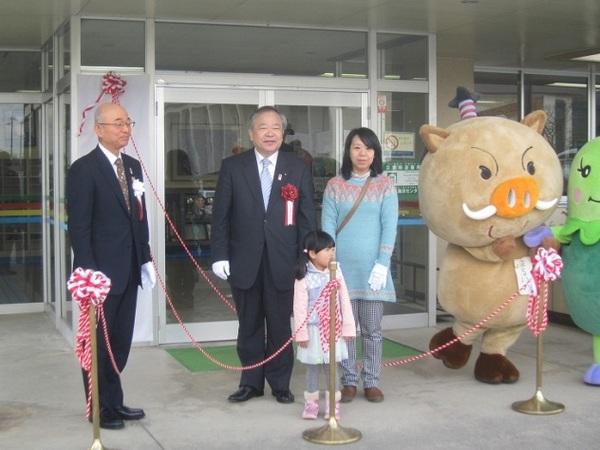 ささやま子育てふれあいセンターの看板の除幕前に市長・副議長・利用者親子・ゆるキャラ2体が並んで写っている写真