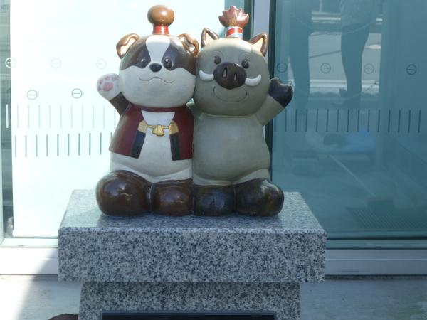 両市のマスコットキャラクター「わん丸君」と「まるいの」が肩を組んで、反対側の手を挙げている丹波焼のオブジェの写真