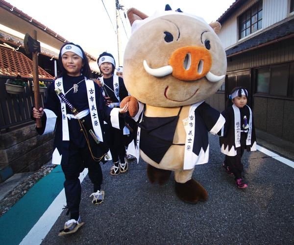 篠山市マスコットキャラクター「まるいの」と手を繋いた女の子達が「子供義士行列」で仲良く歩いている創造農村まちづくり賞受賞の写真