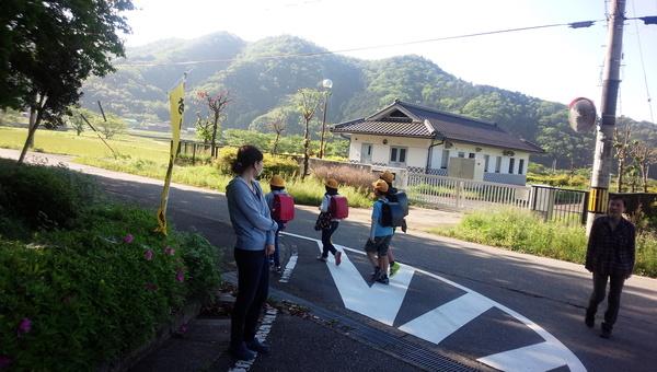 小学生が通り過ぎるのを、見守る保護者の写真