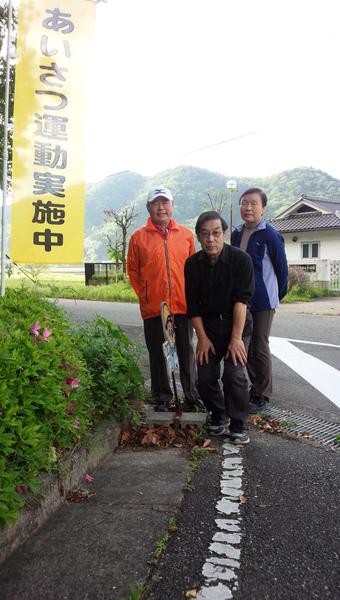 黄色のあいさつ運動実地中の旗と自治会や老人会のみなさんで記念写真