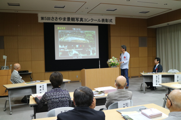 スクリーンに写真を映し、男性が紹介されている写真