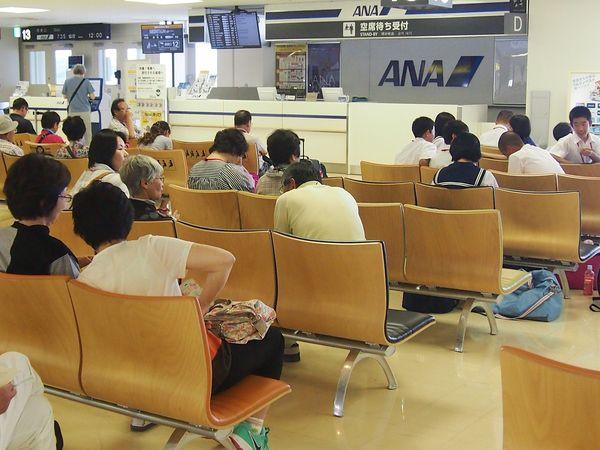 空港のロビー待合席で生徒や関係者が座って待っている様子の写真