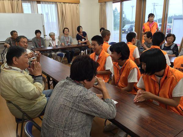 ジュニアボランティアの生徒と住民の方が机を挟んで対面で座っており、笑顔で楽しそうに話をしている様子の写真