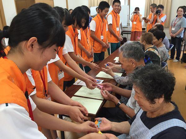 ジュニアボランティアの生徒達が、住民の方に小さいリボンの付いたものを手渡ししている様子の写真