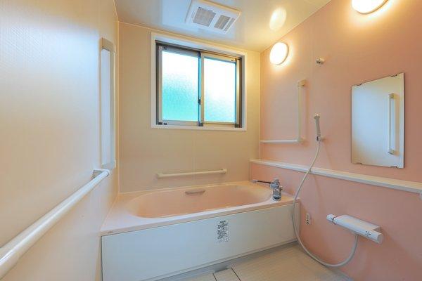 壁の一面がピンク色をした浴槽とシャワーが付いた共同風呂場の写真