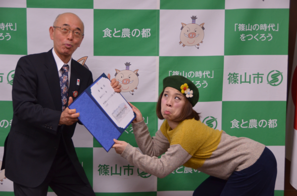市長が変顔をして委任状を森田 まりこさんに渡し、森田 まり子さんがゴリラの真似をして委任状を受け取っている写真