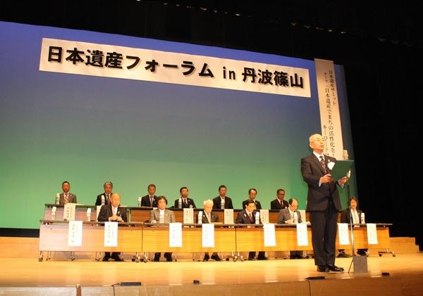 日本遺産フォーラムin丹波篠山と書かれた舞台に2列で作られた机に関係者の人達がすわり中央のマイクで市長が立ちながら話をしている写真